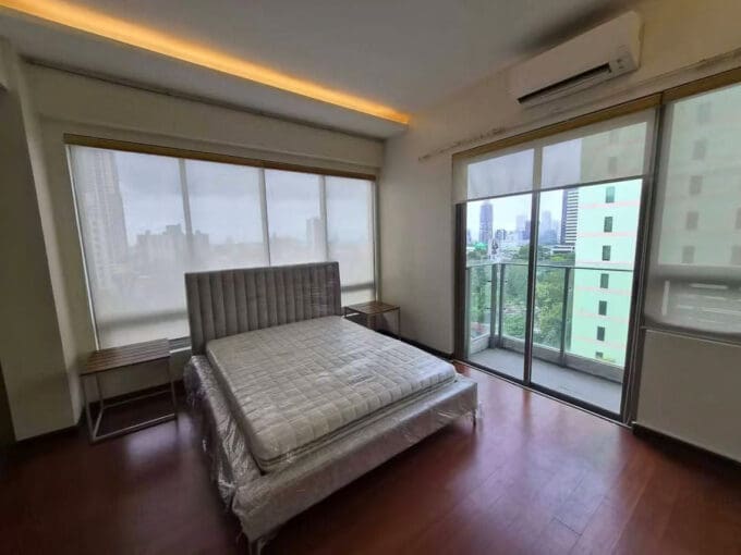 Main bedroom in dark hardwood with an upholstered headboard and a balcony door