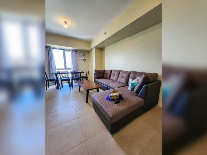 Living and dining area with L-shaped sectional sofa in a furnished 2BR corner unit for sale at Avida Riala Tower 3, Cebu IT Park