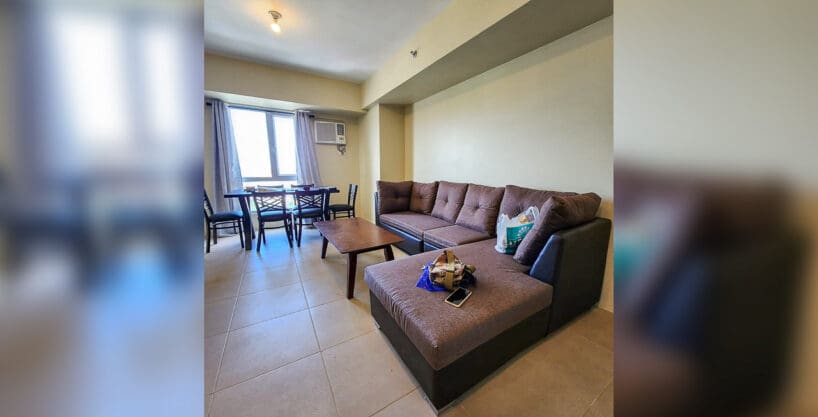 Living and dining area with L-shaped sectional sofa in a furnished 2BR corner unit for sale at Avida Riala Tower 3, Cebu IT Park