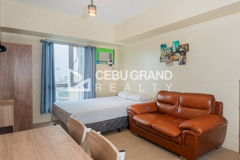 Furnished studio with city view for sale at Avida Riala Tower 3, with the bed by the window and a leather sofa beside it