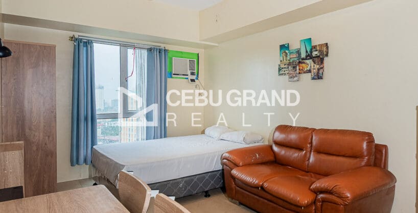 Furnished studio with city view for sale at Avida Riala Tower 3, with the bed by the window and a leather sofa beside it