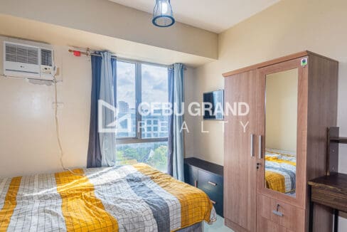 Wall-mounted television, mirrored wardrobe and the bed under the window-type air conditioner