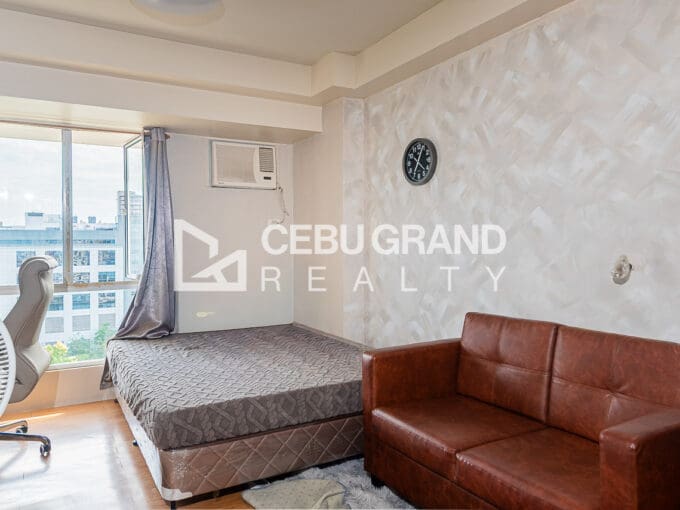 Furnished studio condo for sale at Avida Tower 1, with the bed by the window and a leather sofa against the pearl-textured feature wall