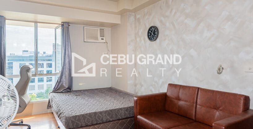 Furnished studio condo for sale at Avida Tower 1, with the bed by the window and a leather sofa against the pearl-textured feature wall