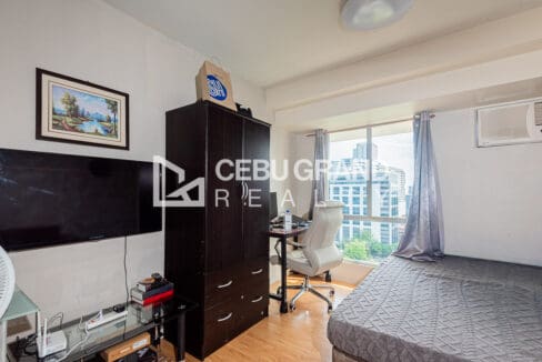 Wall-mounted television, dark timber wardrobe and a desk set into the window bay of the Avida Tower 1 studio