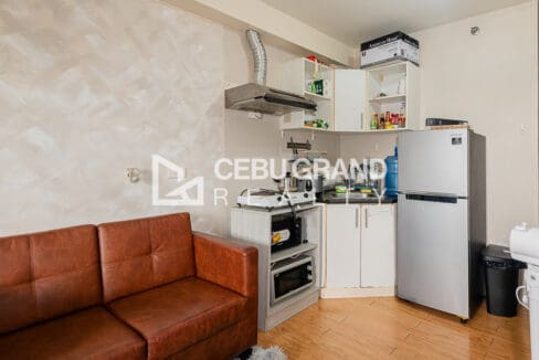 Kitchen corner with white cabinets, range hood, induction hob and a tall refrigerator in the Avida Tower 1 studio