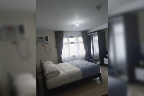 Sleeping area with window-type air conditioning and curtained window in the furnished studio at Galleria Residences