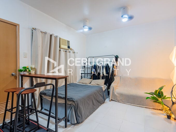 Furnished studio condo for sale at La Guardia Flats, with the bed along the curtained window wall and a bar-height table by the entry