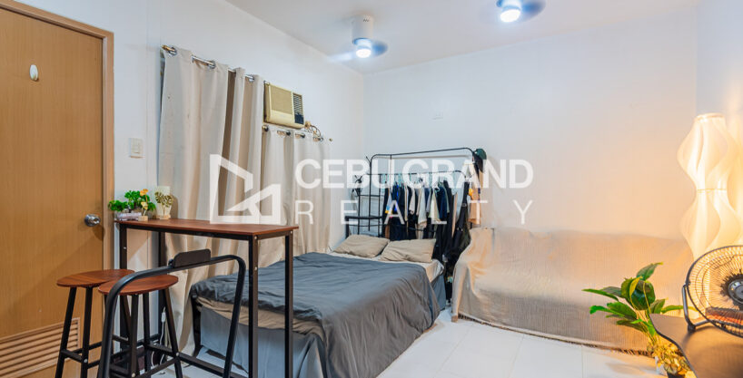 Furnished studio condo for sale at La Guardia Flats, with the bed along the curtained window wall and a bar-height table by the entry