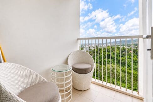 Balcony with two wicker lounge chairs and a glass-top side table overlooking greenery