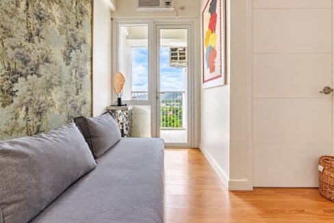 Grey sofa beside the glass door leading to the balcony, with window-type air conditioning above