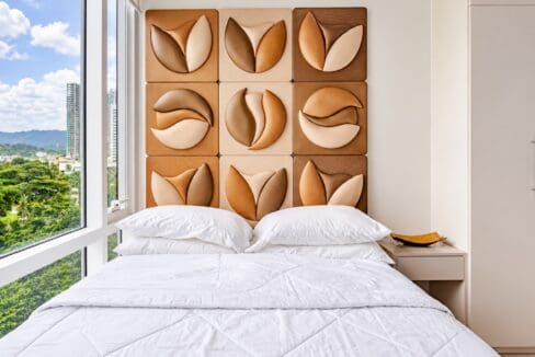 Bedroom with sculpted headboard wall panels, bedside table and floor-to-ceiling window