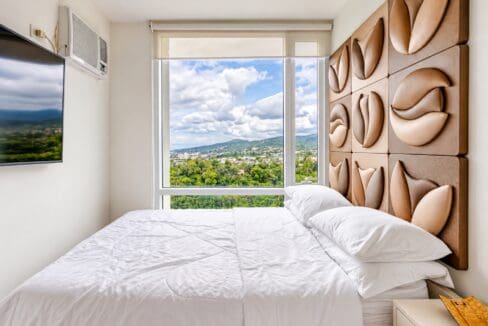 Bed facing a large window with mountain and city views, with wall-mounted TV and air conditioning