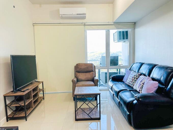 Living area with black leather reclining sofa, recliner armchair and TV console in a furnished 3BR condo for sale at Marco Polo Tower 3, Lahug