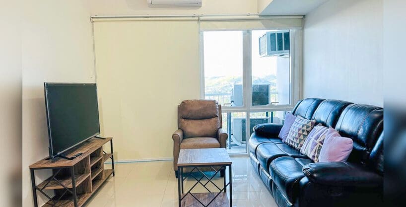 Living area with black leather reclining sofa, recliner armchair and TV console in a furnished 3BR condo for sale at Marco Polo Tower 3, Lahug