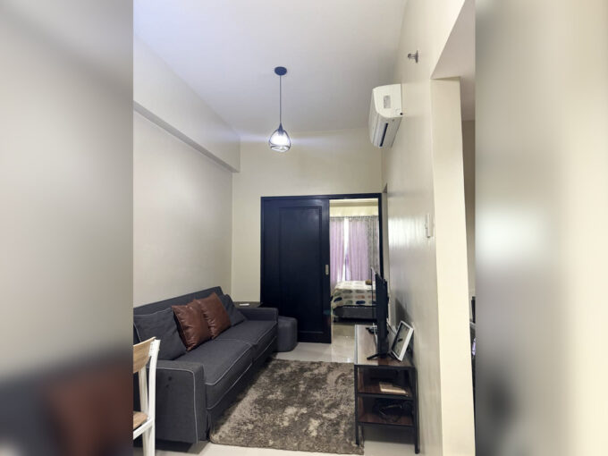Living area of the 1 bedroom condo for sale at One Pavilion with gray sofa, TV console and split-type air conditioning