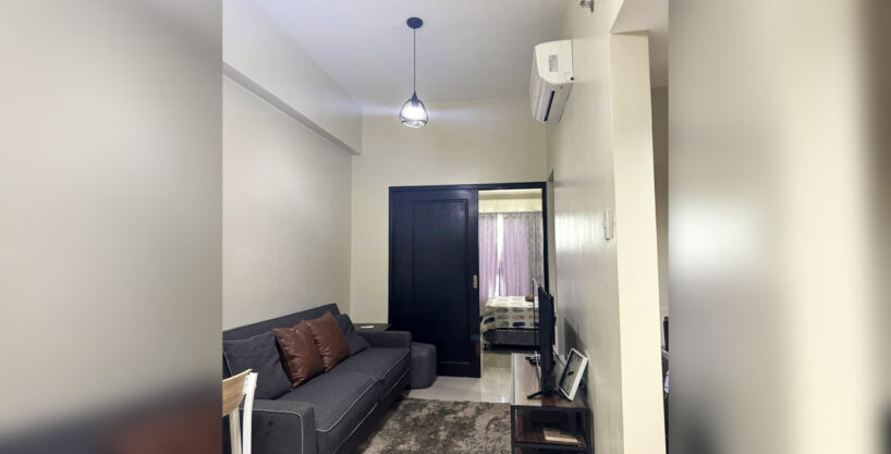 Living area of the 1 bedroom condo for sale at One Pavilion with gray sofa, TV console and split-type air conditioning