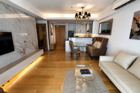 Living area looking toward the entry and kitchen, with the marble-clad television wall lit by a recessed strip