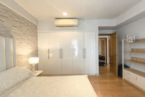 Bedroom with a textured stone feature wall, a full run of white gloss wardrobes and split-type air conditioning