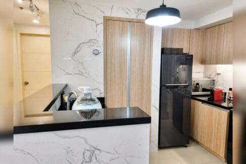 Marble-clad kitchen peninsula with black countertop and refrigerator in the 2BR condo at Solinea Tower 3