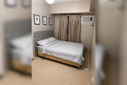 Bedroom with tufted headboard and window-type air conditioning in the 2BR condo at Solinea Tower 3