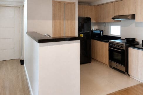 L-shaped kitchen with timber cabinets, black granite counters, and range with hood in the 2BR corner unit at Solinea