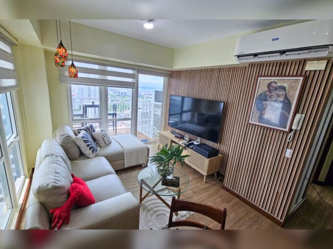 Living area with cream sectional sofa, slatted timber TV wall and balcony door in a 2BR condo for sale at Solinea Tower 2, Cebu Business Park