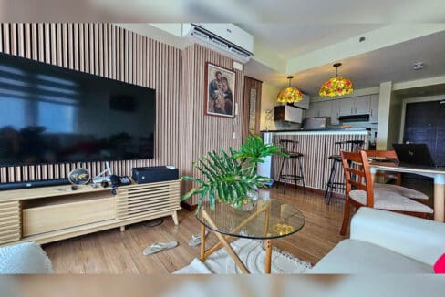 Wall-mounted TV on a slatted timber console, with stained-glass pendant lights over the kitchen counter