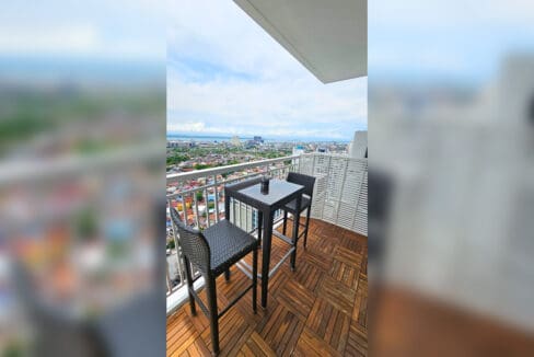 Balcony with timber deck tiles, bar table and two wicker stools overlooking the city and the sea