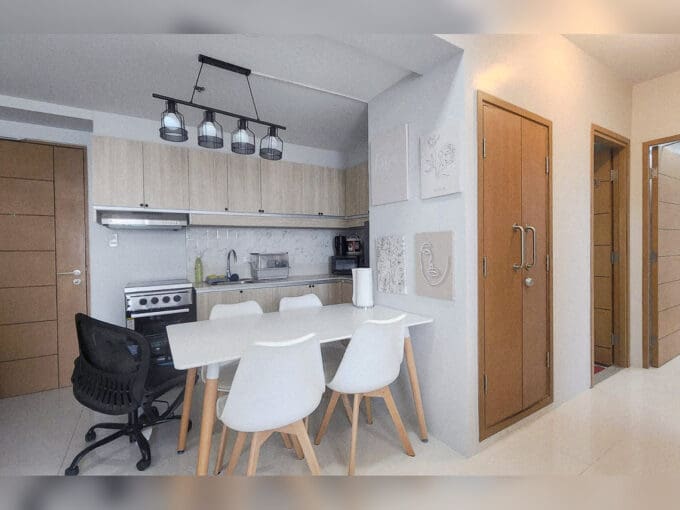Dining table for four under a cage pendant light, with the kitchen behind, in a furnished 2BR condo for sale at Taft East Gate, Mabolo