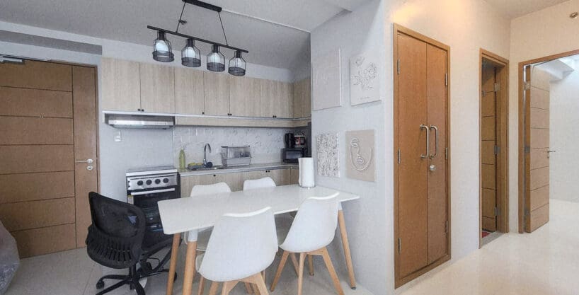 Dining table for four under a cage pendant light, with the kitchen behind, in a furnished 2BR condo for sale at Taft East Gate, Mabolo