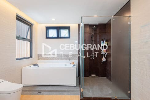 Bathroom with a soaking tub beside a walk-in rain shower in dark tile