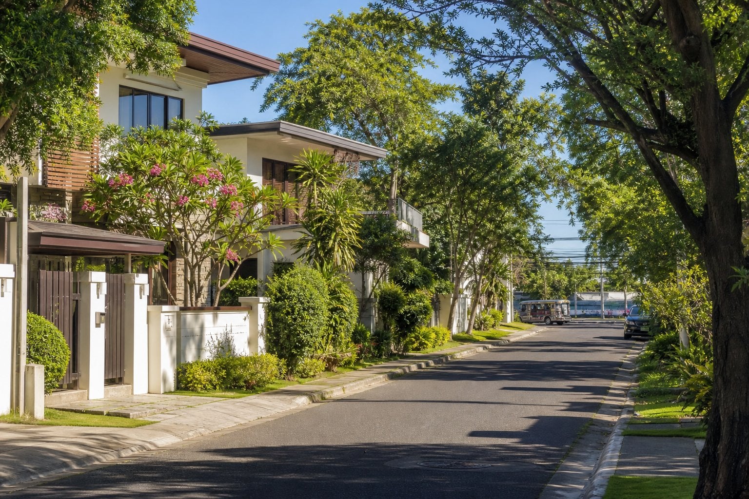 A peaceful leafy residential street in Cebu City with modern homes, tropical greenery, and light traffic in the distance.