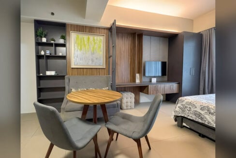 Round wood dining table, grey chairs and wood-panel TV wall in the Asia Premier studio