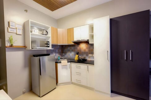 Kitchenette with patterned backsplash, range hood, microwave and refrigerator in the Avida Riala studio