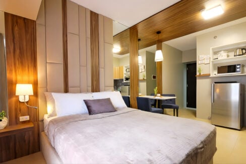 Upholstered headboard wall and reading lamp with the dining area behind in the Avida Riala studio