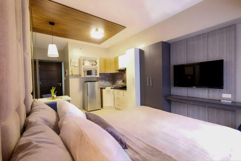View from the bed to the kitchenette, wardrobe and wall-mounted TV in the Avida Riala Tower 1 studio