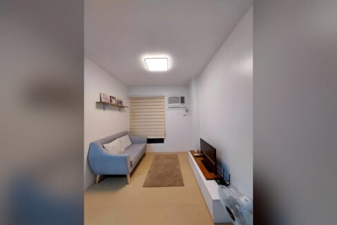 Living area with grey-blue sofa, shag rug and TV console in the Avida Tower 2 one-bedroom