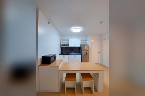 Kitchen with white cabinets, two-door refrigerator and dining counter with two stools at Avida Tower 2