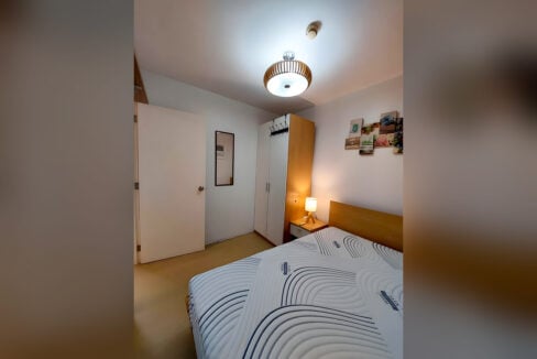Bedroom with wood-slat pendant light, wardrobe and wall mirror in the Avida Tower 2 one-bedroom