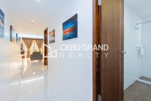 Hallway with marble-look tiles and framed art leading to the living room