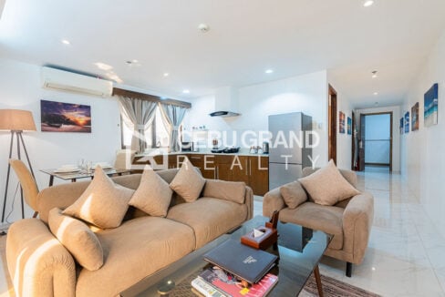 Beige sofa and armchair with the kitchen and art-lined hallway behind