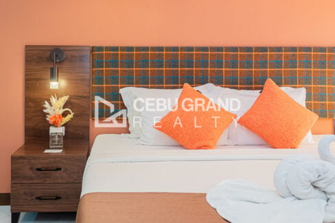 Plaid headboard, orange cushions and a walnut nightstand with reading light