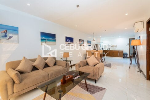 Living room with a sofa and armchair, glass coffee table and kitchen beyond