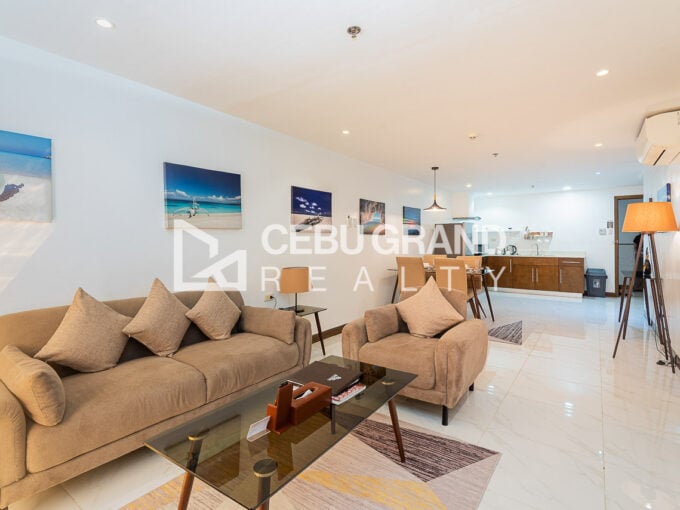 Living room with a sofa and armchair, glass coffee table and kitchen beyond