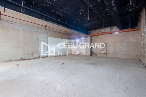Bare shell interior with a concrete floor, block walls and exposed ceiling pipes
