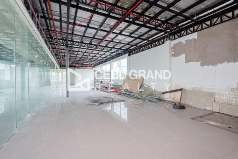 Long open floor beside a glass partition, under exposed steel trusses and sprinkler lines
