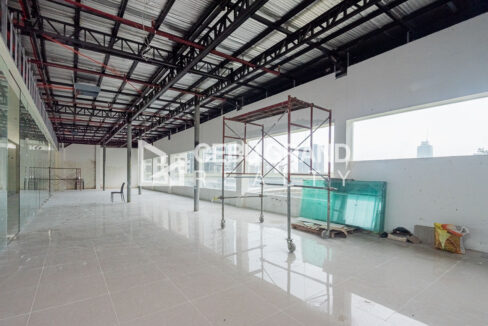 Long open floor under a steel-truss roof with wide windows facing the city high-rises