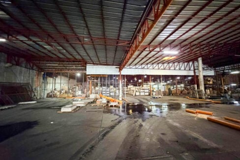 Wide concrete floor under red steel roof trusses and skylight panels