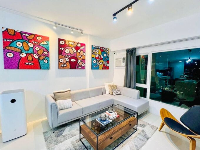 Living area at Park Tower 1 with an L-shaped grey sectional, glass coffee table and colourful wall art